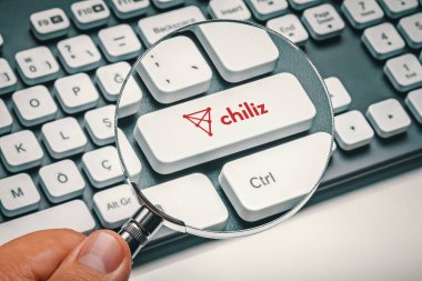 Kripto para ticareti kavramı: Büyüteç tutan erkek el ve kırmızı biberli bilgisayar anahtarı; chz altcoin logosu. Kripto para birimi madenciliği, ticaret, pazar konsepti.