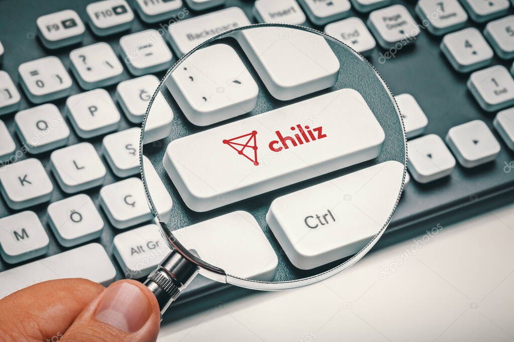 Cryptocurrency trading concept: Male hand holding magnifying glass and focusing computer key with chiliz | chz altcoin logo. Cryptocurrency mining, trading, market concept.