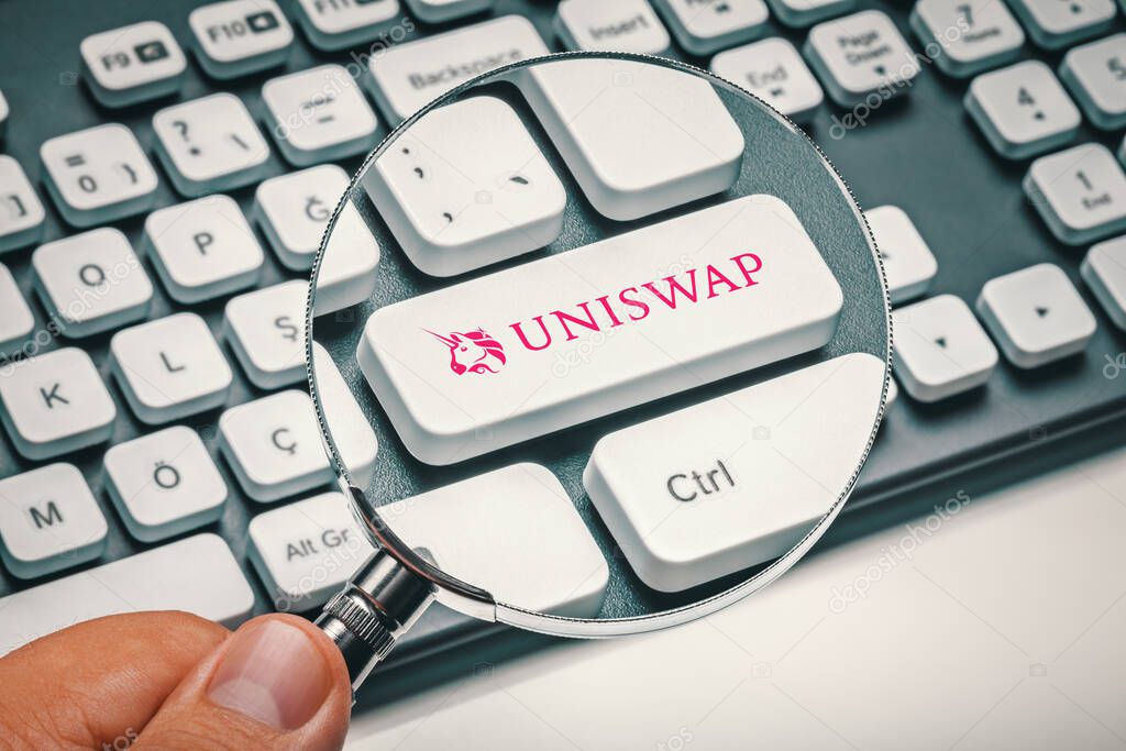 Cryptocurrency trading concept: Male hand holding magnifying glass and focusing computer key with uniswap | uni altcoin logo. Cryptocurrency mining, trading, market concept.
