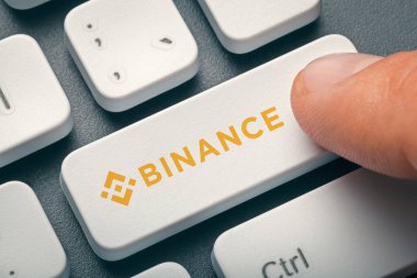 İşaret parmağı basılı bilgisayar anahtarı ve binance bozuk para logosu. Kripto para birimi madenciliği veya ticaret konsepti.