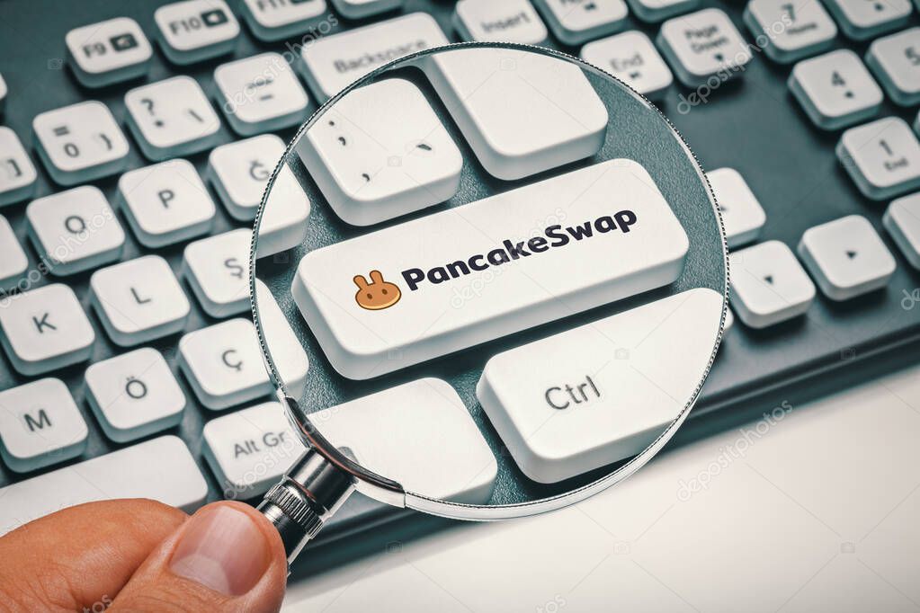 Cryptocurrency trading concept: Male hand holding magnifying glass and focusing computer key with pancakeswap altcoin logo. Cryptocurrency mining, trading concept.