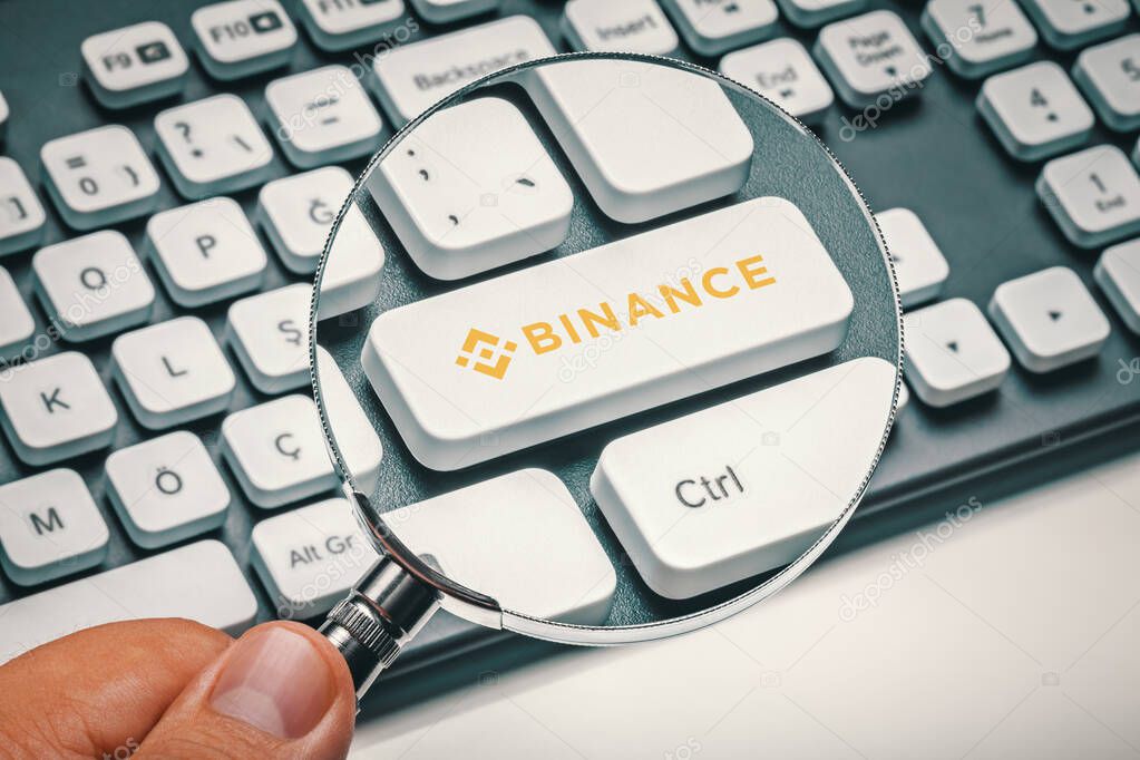 Cryptocurrency trading concept: Male hand holding magnifying glass and focusing computer key with binance coin logo. Cryptocurrency mining, trading concept.