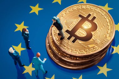 Bitcoin konsepti için yatırım kararı hakkındaki iş toplantısı: Avrupa Birliği bayrağında parlak altın bitcoin yığınının yanında duran minyatür işadamı figürleri.