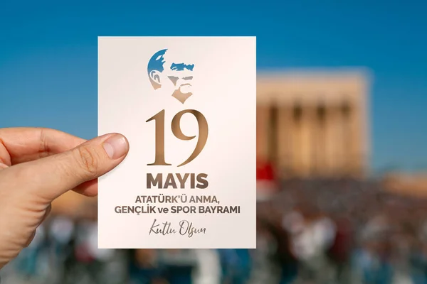 19 Mayıs kutlama mesajı olan beyaz bir tebrik kartı tutan bir erkek. İngilizce: Mutlu 19 Mayıs, Atatürk, Gençlik ve Spor Günü.