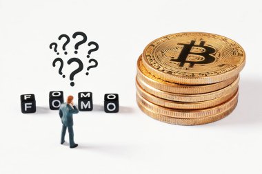 Beyaz arkaplanda FOMO metni olan dağınık siyah küpler. Kafasının üstünde soru işaretleri olan bir iş adamı figürü. Bitcoin yığınının yanındaki küplere bakıyor. Kripto para birimi, engelleme zinciri veya ticaret konsepti.