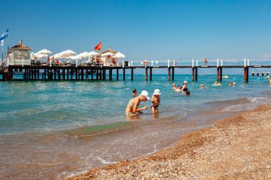 Antalya, Türkiye-29 Haziran 2021: Anne ve tatlı kız denizde oyun oynuyorlar. İnsanlar denizde yüzüyor, Antalya 'da yazın tahta iskelede güneşleniyor. Coronavirüs salgını sırasında yaz tatilindeki turistler. 