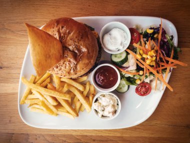 Soslu lezzetli hamburger, yeşil salata, Rus salatası ve patates kızartması restoranda masada servis ediliyor..