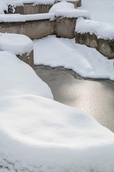 Rochas cobertas de neve perto da lagoa no parque — Fotografia de Stock