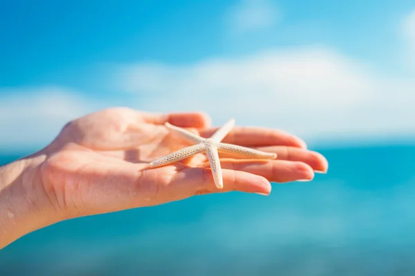 Palma femminile con grandi stelle marine arancioni davanti al cielo blu e al mare — Foto Stock