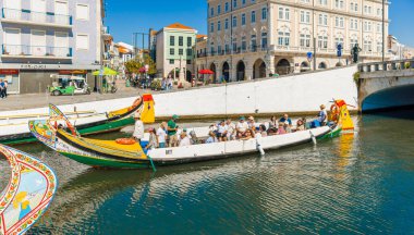 AVEIRO-PORTUGAL: 13 Ekim 2025: Turistlerle dolu renkli moliceiro tekneleri, Aveiro 'nun kanalı boyunca tarihi bina ve mağazalar zeminine doğru hareket ediyor