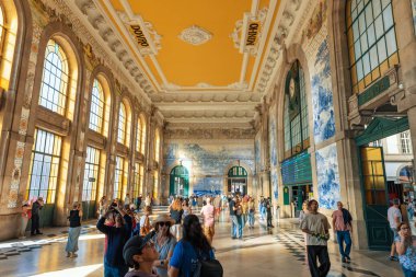 PORTO-PORTUGAL: 13 Ekim 2025: Porto, Portekiz 'deki Sao Bento tren istasyonunun büyük salonu içindeki turistler ve gezginler, dekoratif mimari ve fayans sanatına hayran kaldılar. Meşhur mavi azulejo fayans duvarları ve güneş ışığı içeri akıyor..