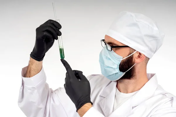 A male laboratory assistant examines a green substance in a test tube. A male scientist in a white lab coat holds a bottle of green chemical liquid. Laboratory testing of cosmetics.