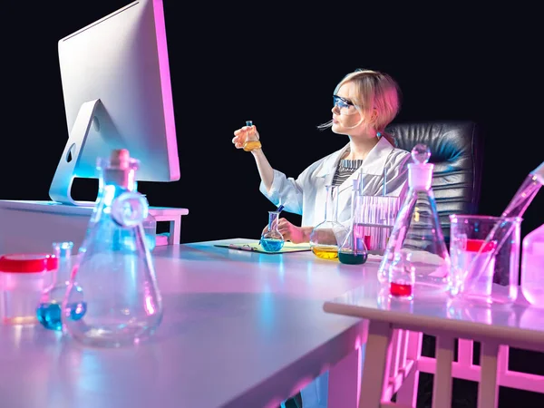 Computer next to chemistry teacher. Woman in the uniform of a laboratory assistant in front of monitor. Concept - it broadcasts experiments through a computer. Laboratory glassware on chemist table.