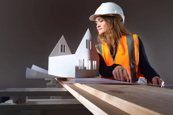 Architect woman smile. Architect woman looks at layout of house. Girl in uniform of a builder. Young lady builder sits on a black background. Concept - she works in an architectural bureau.