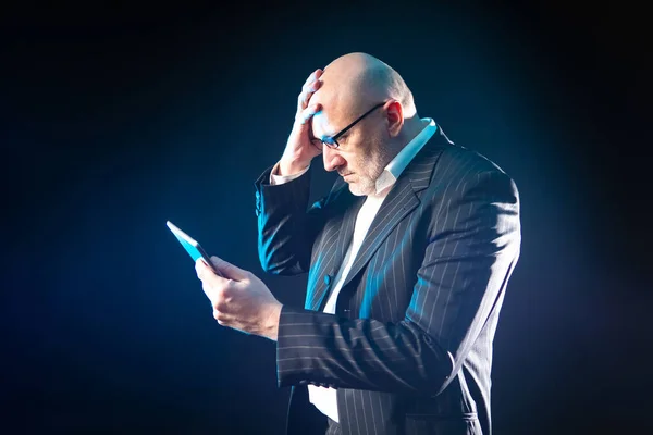 Human is holding his head. Concept - a man learned bad news. A businessman learned bad news from the phone. Adult man on a dark background. The businessman is upset. Upset man with telephone