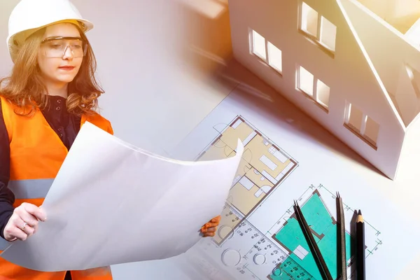 Girl next to the construction drawings. Woman holds room plans in her hands. Concept - woman builder. Girl works in a construction office. Architect's desk. Concept - drawing up room plans.