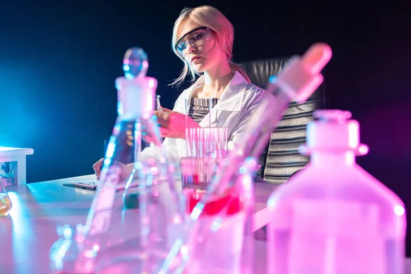 Test tubes in front of the laboratory assistant. Girl scientist in a dark laboratory. The laboratory assistant works while sitting in a chair. Concept - she is engaged in scientific research.