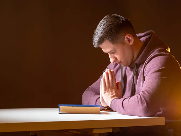 Man prays at the table. Person is sitting at a table with a Holy Bible. Man turns to God. Religion and faith. The crisis of Christian life. Prayer for God\'s blessing. Beg for forgiveness.