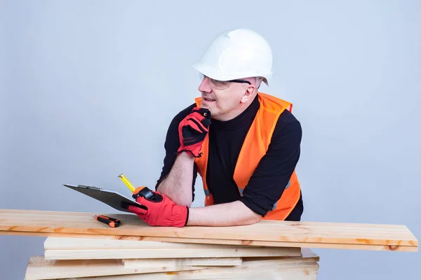 The carpenter looks away and smiles. A man in a construction helmet leans on the boards. Woodworking. Joinery. Working with lumber.