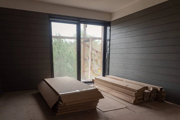 Construction of a country house. Room of a cottage under construction in a pine forest. Construction materials in a renovated room. Packs of laminate and wall panels in the room.