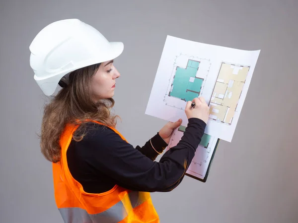 Female student architectural college. Woman with construction drawings on a gray background. Woman in orange vest and a helmet. She is studying to be architect. Girl prepares architectural drawings