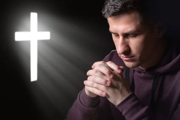 Appeal to religion. A man prays to God. Praying man on the background of the cross. A Catholic asks for help from God. God\'s help and grace.