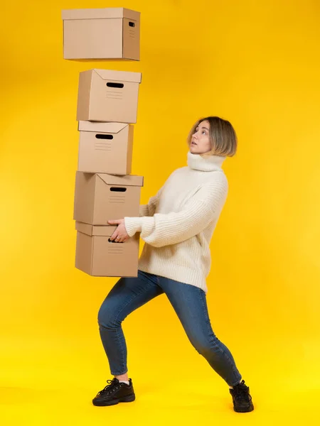 Multitasking concept. A girl with several cardboard boxes in her hands catches another box. Metaphor - a huge number of tasks in the work. A lot of things. Woman is engaged in business.