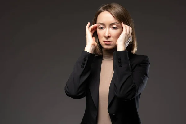 Stress at work. Woman shows that she is stressed. Business woman on a dark background. Girl is stressed at work. She keeps her hands near her head. Stress at work at an office worker