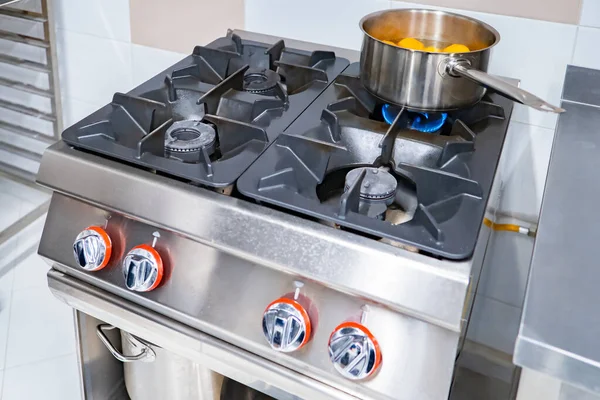 Chrome gas stove. Professional gas stove in restaurant kitchen. Ladle with something on gas stove. Dish is being prepared. There is something to cook in metal ladle. Hot food processing in restaurant