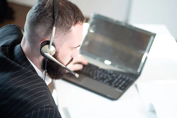 Call center agent with a headset on his head. Call center agent close up. Support agent works with a laptop. Man takes calls through a laptop. Call center employee during work. Office worker.