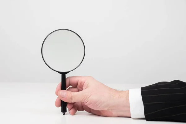 Man holds a magnifying glass. Man shows a magnifier. Concept - it shows something under a magnifying glass. Businessman shows a magnifying glass. Magnifier as a symbol of audit. Consideration.