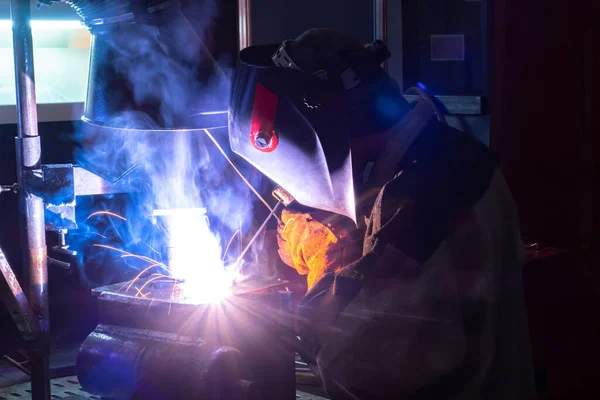 Portrait of a welder at work. A man with a welding machine in the dark. A man in a welding mask with his back to the camera. It works hot welder. Welder metal with arc welding machine