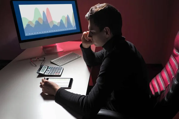 Investor at work. Man invests in stock exchange. Investor next to a computer or tablet. Young guy is investing over Internet. Stock growth graph on a computer monitor. Tender career.