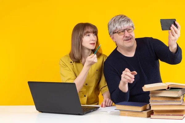 Man and a woman make a video call. Satisfied guy and girl. Mature man and a female student on a yellow background. Teacher and student during video call. They make a video call through phone