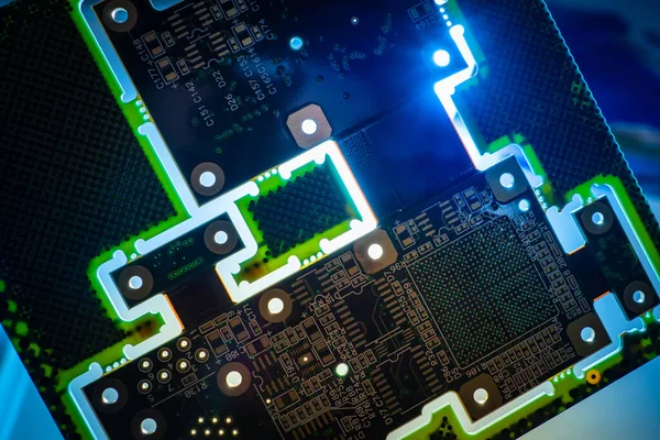 Circuit board close-up. Dark PCB glows in dark. Background consists of a piece of PCB. Computer board with luminous paths. High-tech manufacturing concept. Light passes through holes in PCB