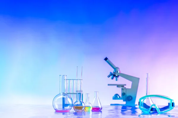 Flasks, a microscope, and safety glasses on a blue background. Chemical equipment near the place for the text. medical glassware and plastic safety glasses in scientific lab.
