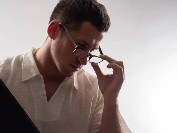 Man teacher adjusts his glasses. Portrait of a guy working as a lector. Guy on a white background. Man teacher is thinking about something. Pensive Man teacher. He teaches at school or college