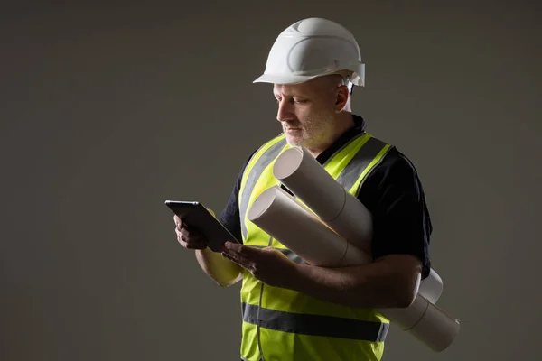 Builder worker with tablet in his hands. Adult builder worker on dark background. Man builder worker is looking for something in electronic tablet. App concept for builders. Construction app