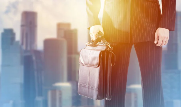 Sunrise and downtown behind a businessman. Man with a business briefcase. Concept - sale of business briefcase. Business clothing and accessories. Background on topic of doing businesslike.