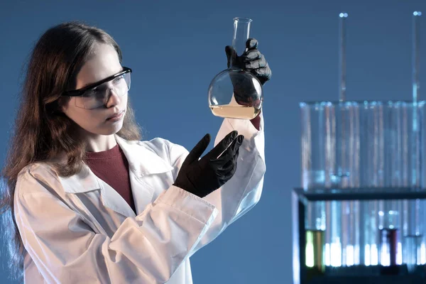 Student in laboratory. Young woman in a laboratory coat. She holds and examines test tube. Concept - University laboratory. Student is engaged in scientific research. She experiments with reagents