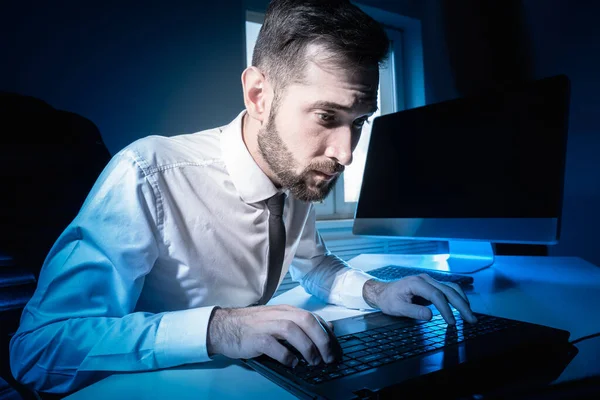 An office worker works overtime. Portrait of an office worker working at night. Close-up of man who is printing something. Concept - person is forced to work in overtime. Manager in a dark office.