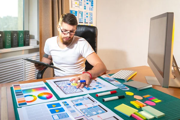 UX designer at work. He draws app layouts on paper. UX designer career. Application development process. Creation of applications in design studio. Designer at desk. Web application design