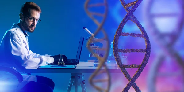 Geneticist with laptop and micras. DNA helix next to laboratory assistant. Geneticist at his desk. Geneticist is considering DNA helix. He is studying science of genetics. Concept genetic business