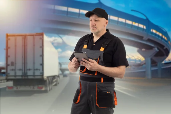 Automotive logistics. Logistics man with tablet. Concept - work as dispatcher-logistician. Employee of logistics company. Blurred truck under bridge in background. Dispatcher-Logistician career.