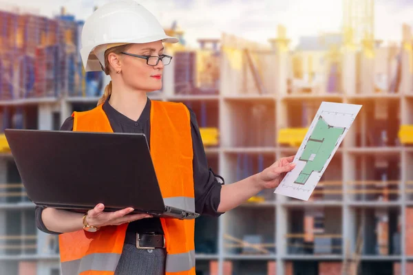 Woman builder with construction drawings in her hands. Woman works a large construction site. Builder with a laptop in his hands. Architect on background of high-rise building under construction.