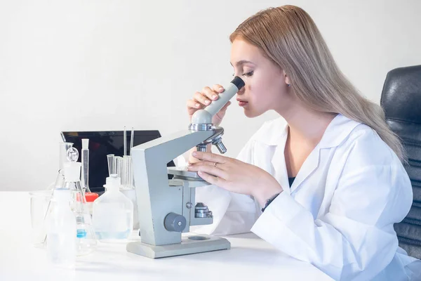 Woman in science laboratory. Laboratory assistant with microscope. Research career. Girl scientist in white coat. Test tubes and microscope on chemist\'s table.  chemist is doing research.