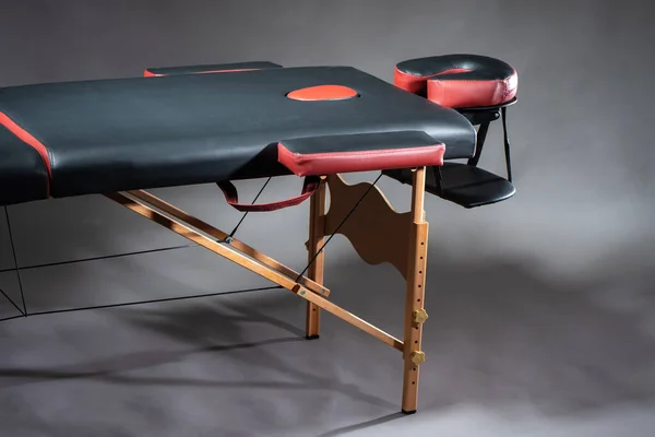 Massage table on a gray background. Ergonomic furniture for massage rooms. Workplace of the masseur. Massage couch with armrests and headboard.