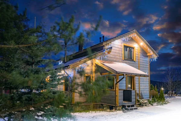 Country hotel. Wooden house in winter weather. Country hotel on background of night sky Wooden two-storey house.  facade of cottage is illuminated with garlands. Home for winter vacation.