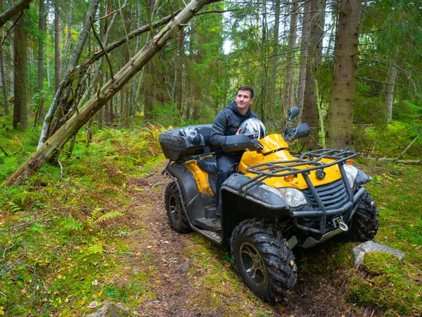 Man on a quad bike. ATV driver in the forest. A portrait of an quad bike driver. Concept - riding an ATV. Active rest of the quad bike. Riding a quad bike off-road. Man on yellow ATV