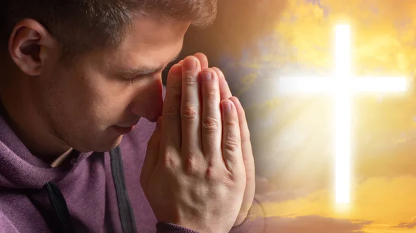 Catholic is praying. Believer man next to cross. Religious cross in front of guy. Christian is praying with folded palms. Catholic cross on sky background. Catholic religion. Rite of prayer to God.